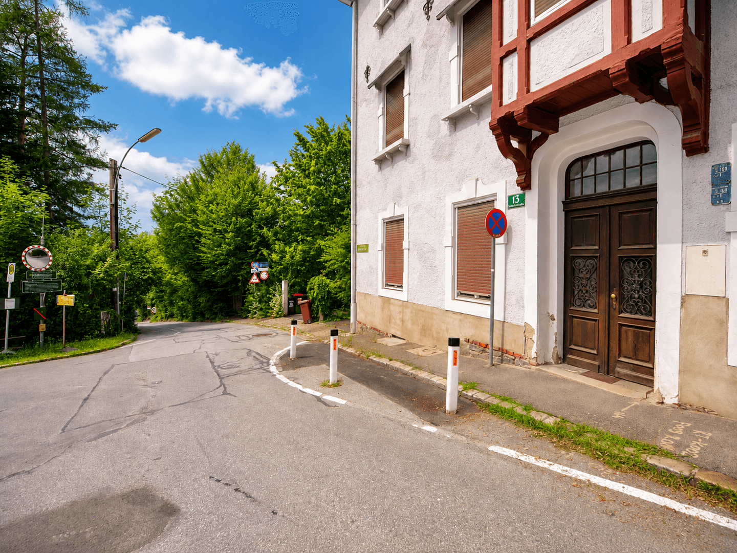 Historisches Gebäude mit Holzbalkon und brauner Eingangstür an einer ländlichen Straße.