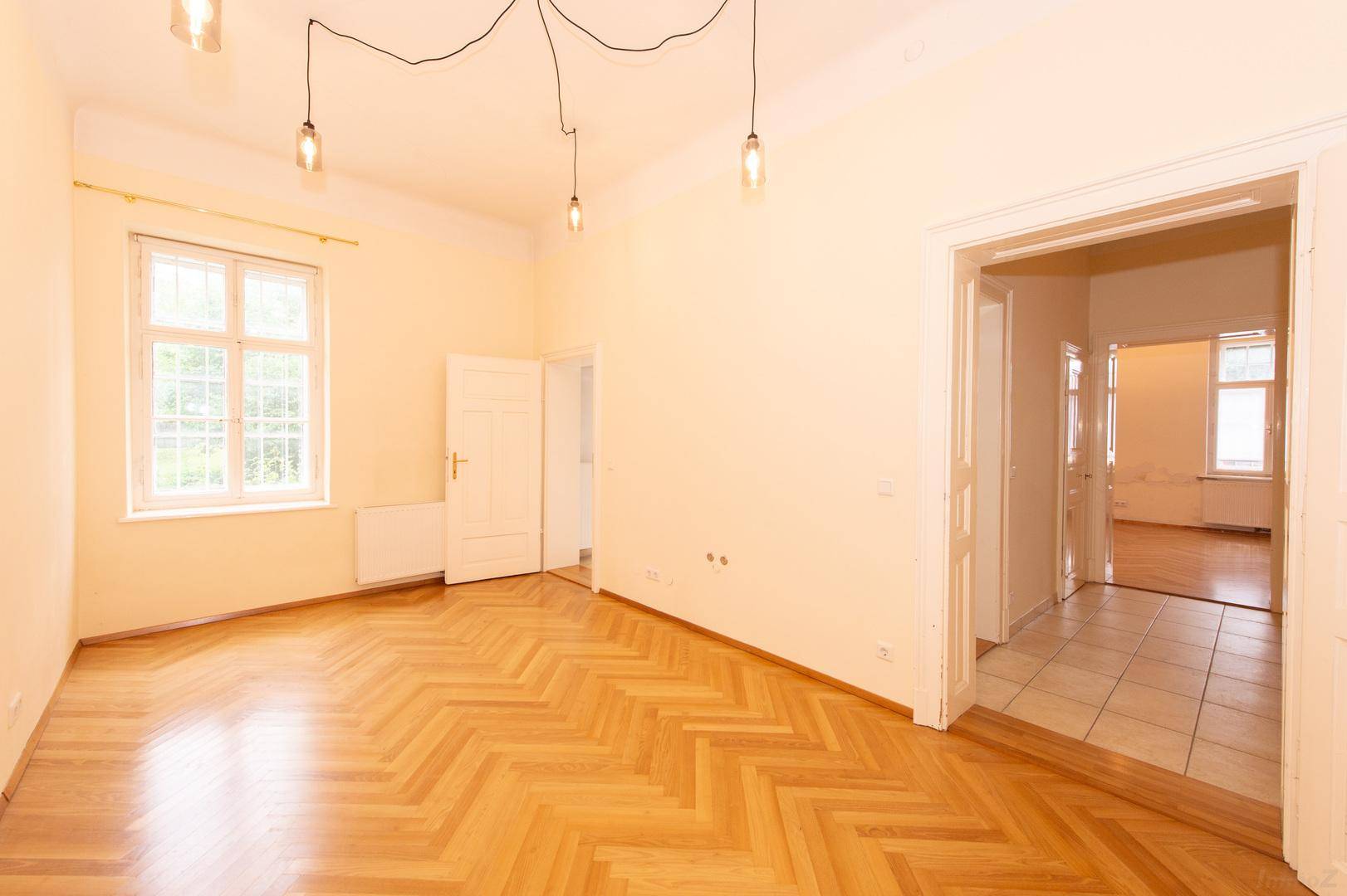 Geräumiges Zimmer mit Fischgrätparkett, hohen Decken und großen Fenstern für viel Licht.