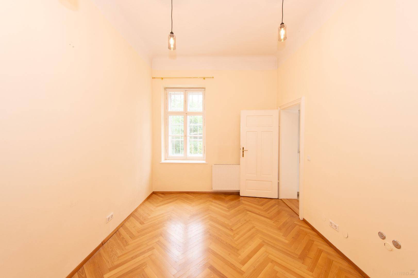 Helles Zimmer mit klassischem Fischgrätparkett und einem großen Fenster für viel Tageslicht.