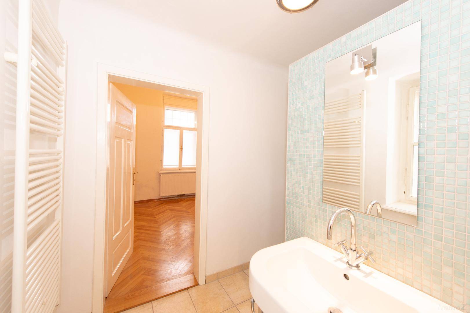 Helles Badezimmer mit Waschbecken, Spiegel und Blick in den angrenzenden Wohnbereich.