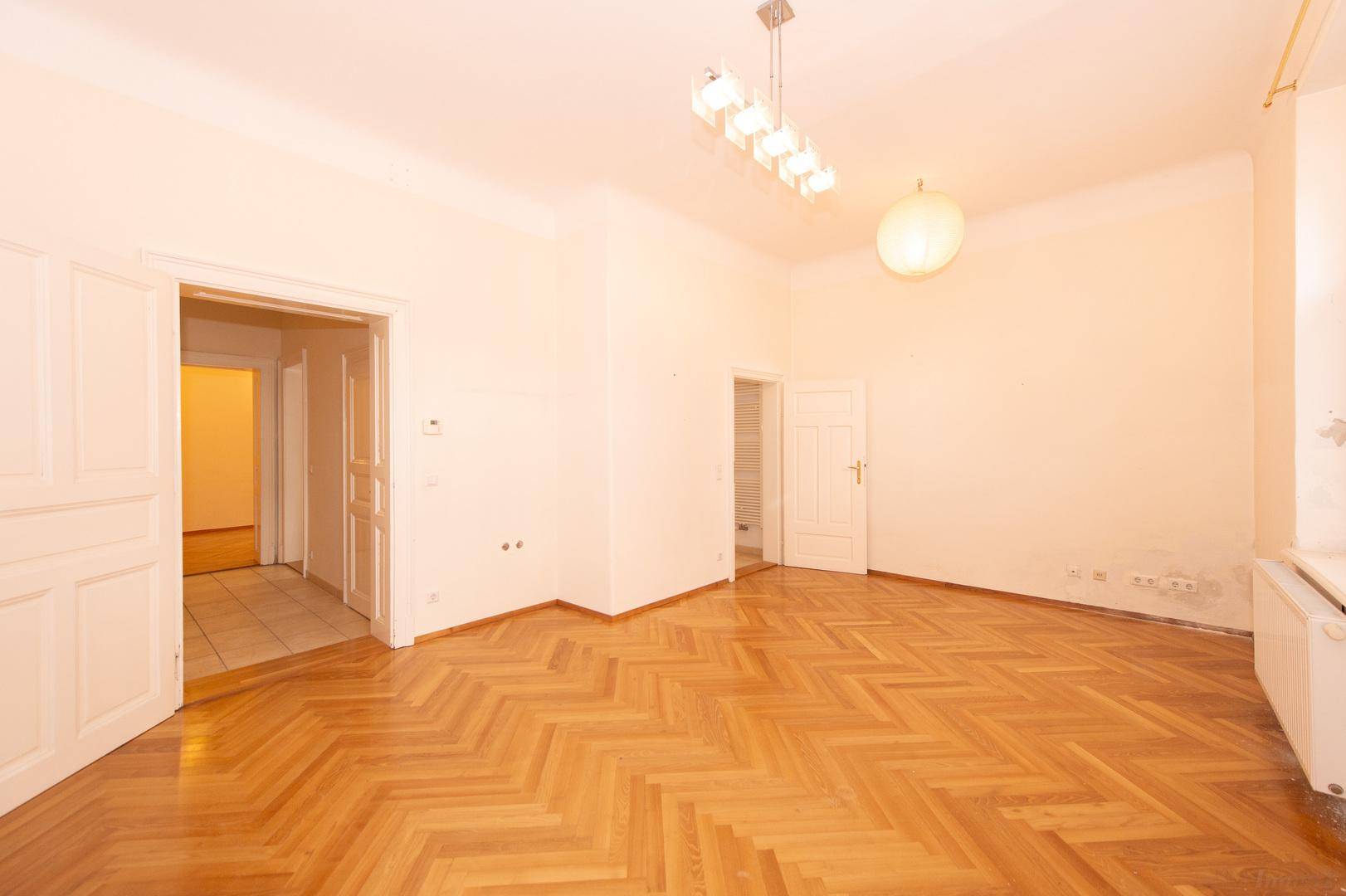 Heller Wohnraum mit Fischgrätparkett und offenem Zugang zum Flur der Wohnung.