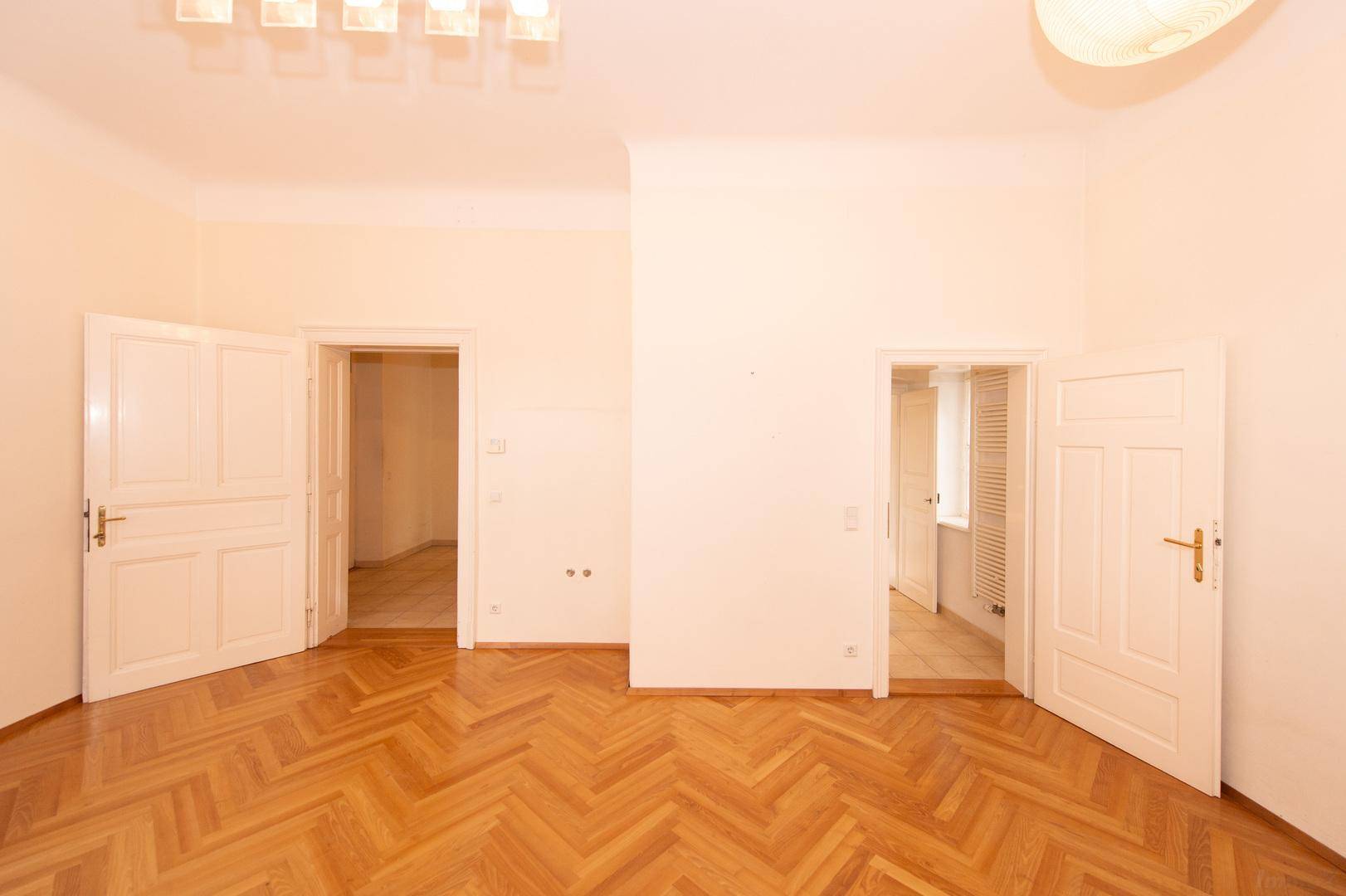 Geräumiges Zimmer mit Fischgrätparkett und mehreren Türen zu angrenzenden Räumen.