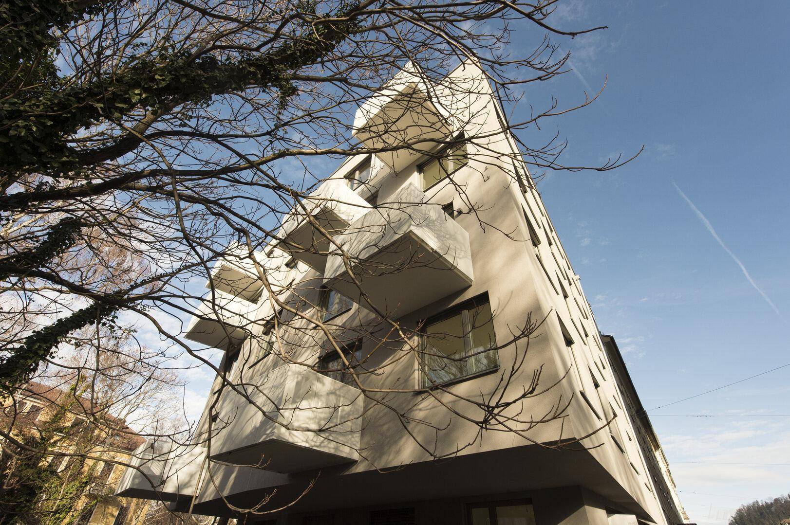 Moderne Architektur mit markanter, eckiger Fassade und kleinen Balkonen unter blauem Himmel.