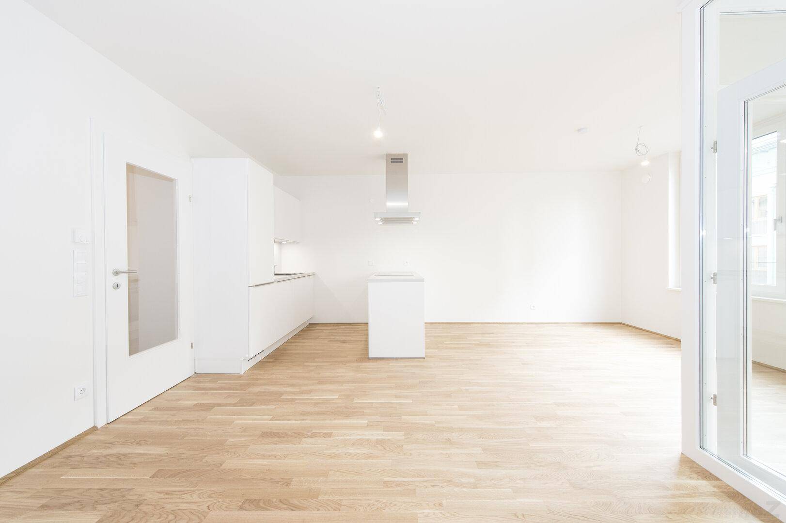 Geräumiger, heller Wohnbereich mit integrierter Küche, Holzboden und viel Tageslicht.