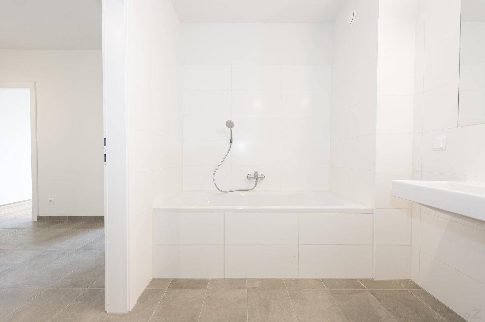 Modernes Badezimmer mit eingebauter Badewanne und Handbrause, gefliest in hellen Tönen.