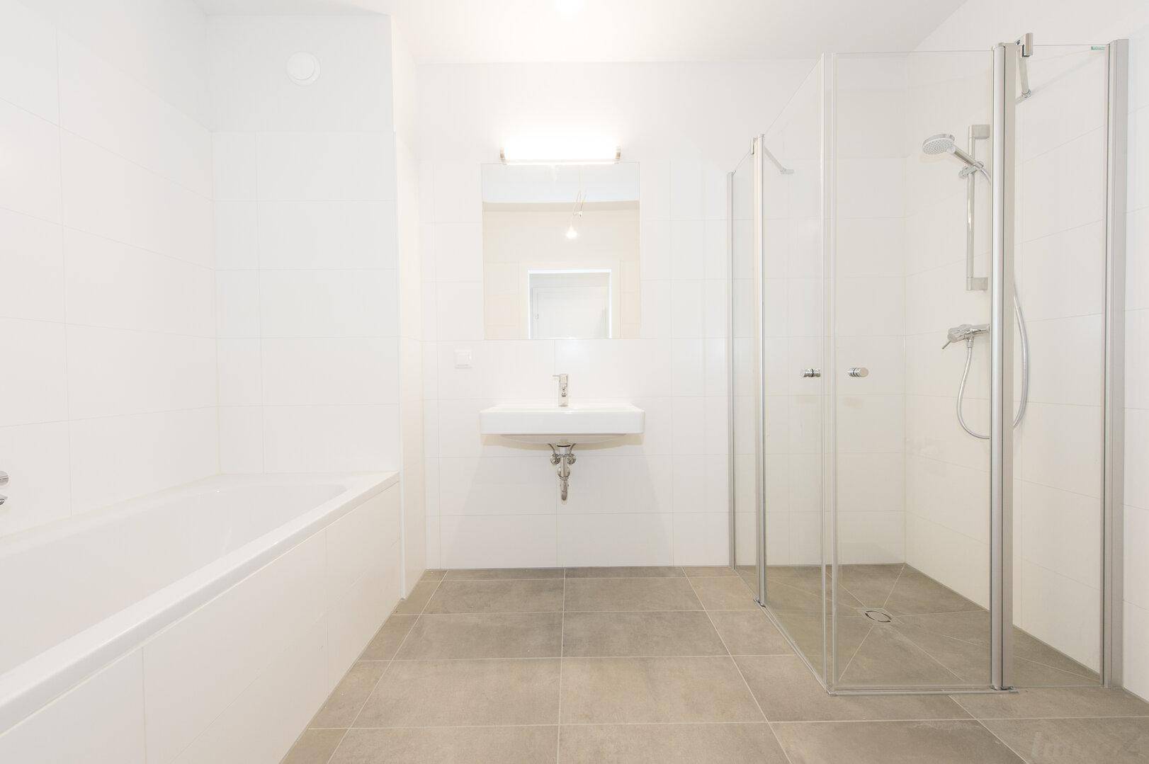 Helles Badezimmer mit Badewanne, Duschkabine, Waschbecken und großformatigen Fliesen.