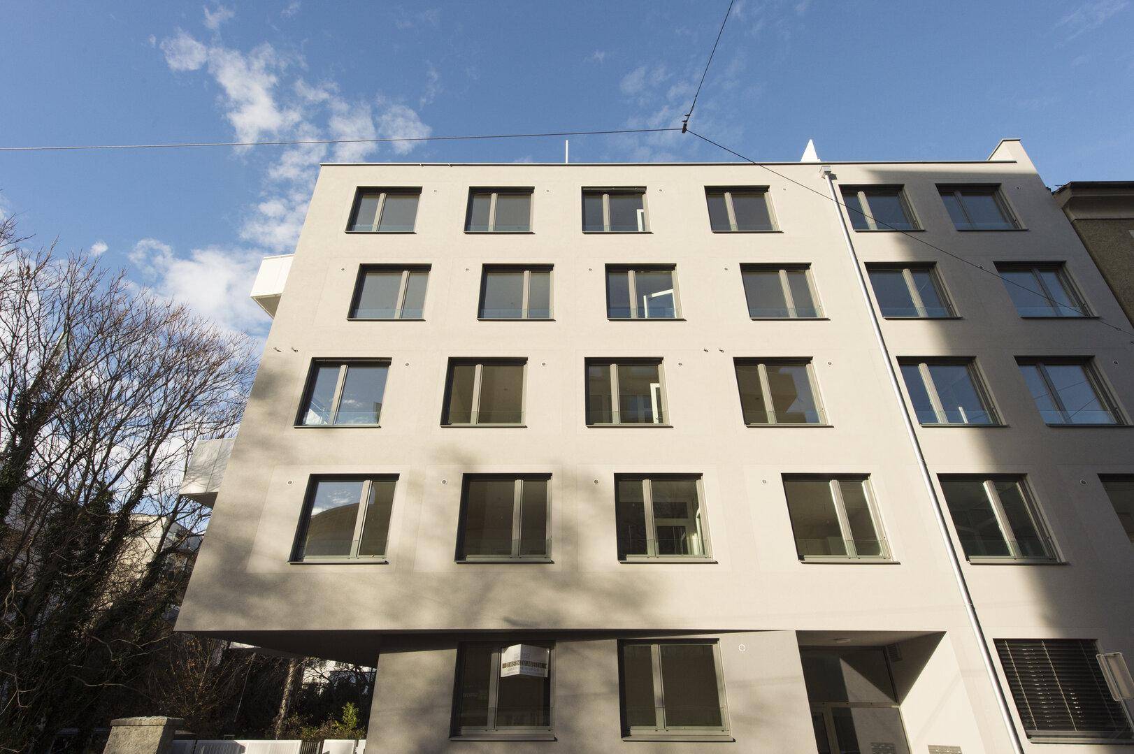 Moderne Fassade eines Mehrfamilienhauses mit vielen Fenstern unter blauem Himmel.
