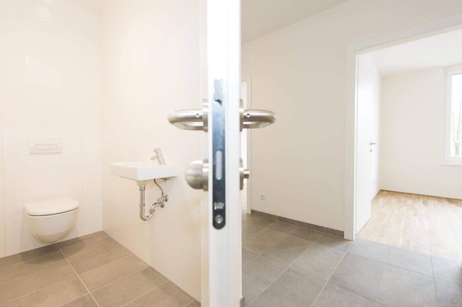 Modernes Gäste-WC mit wandhängender Toilette und kleinem Waschbecken, hell gefliest.