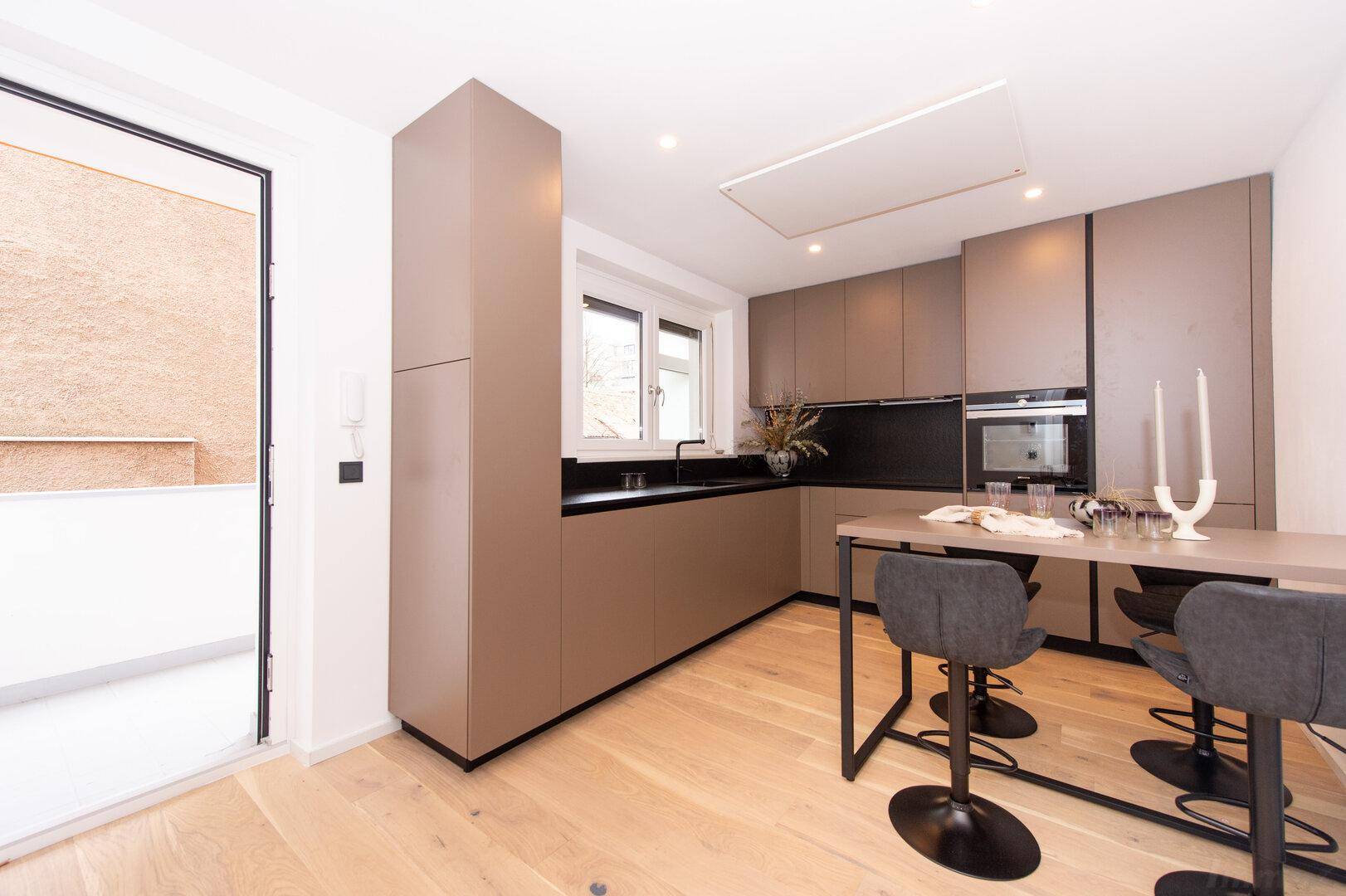 Helle Küche mit Zugang zu einem Balkon, ausgestattet mit modernen Geräten und Holzboden.