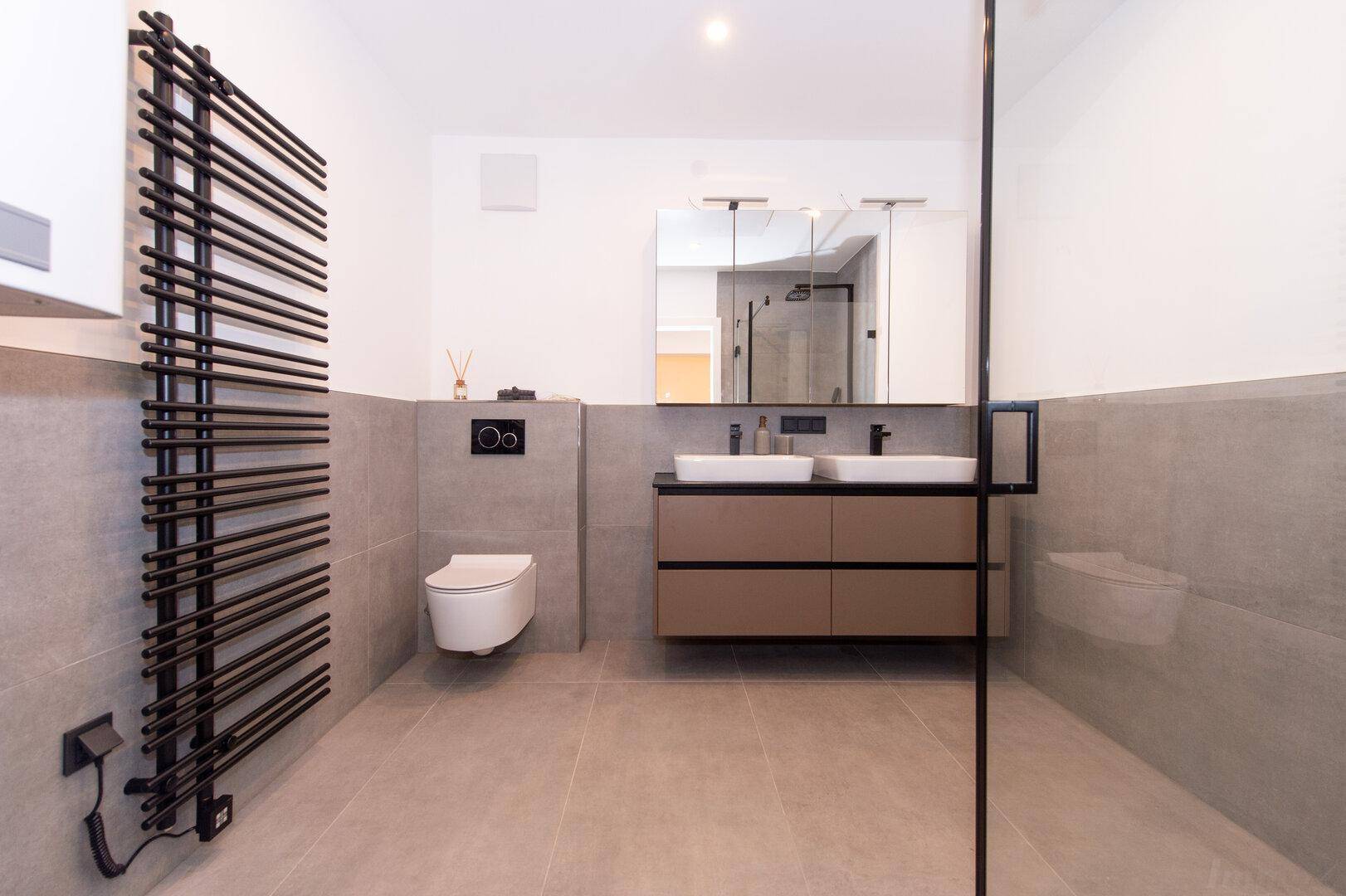 Modernes Badezimmer mit Doppelwaschbecken, wandhängendem WC und beheiztem Handtuchhalter.