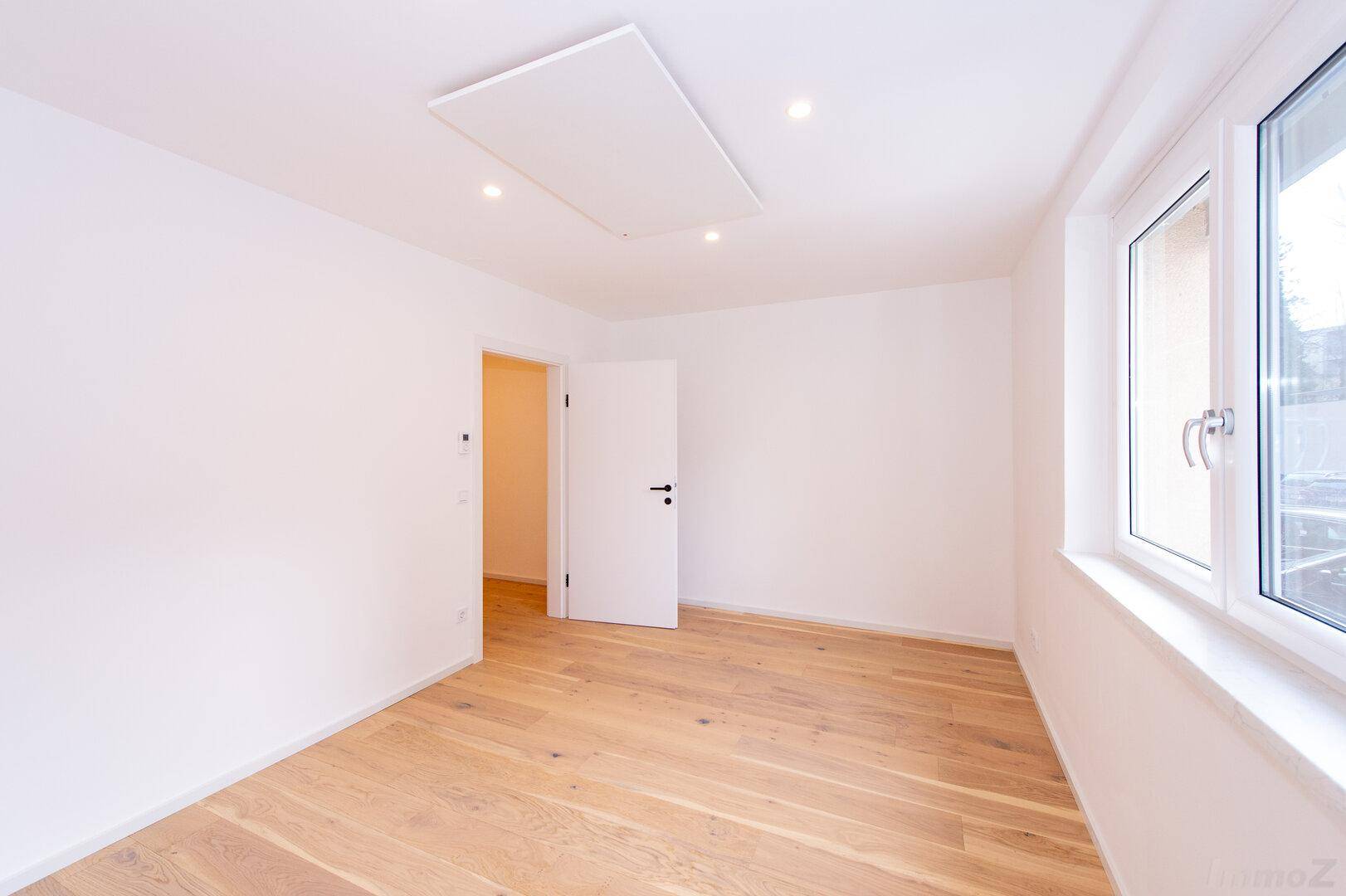 Helles Schlafzimmer mit Holzboden und großem Fenster, bereit zur individuellen Gestaltung.