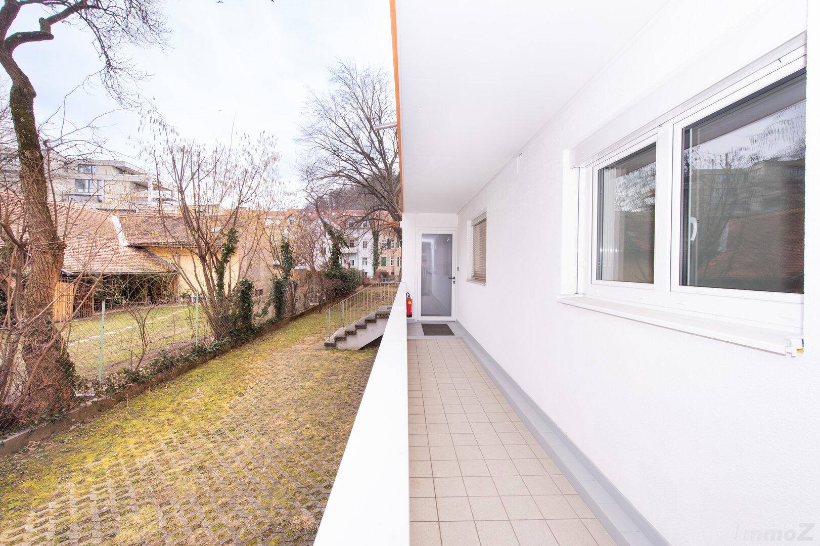 Balkon mit Blick auf einen begrünten Hinterhof und angrenzende Gebäude.