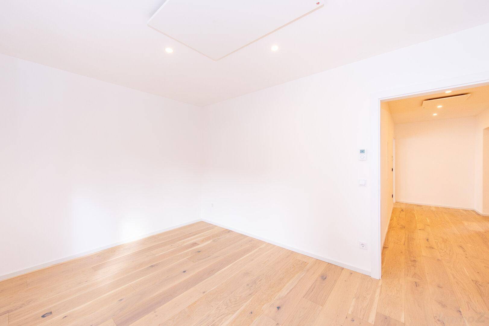 Leeres Zimmer mit Holzboden und weiß gestrichenen Wänden, bereit zur individuellen Nutzung.
