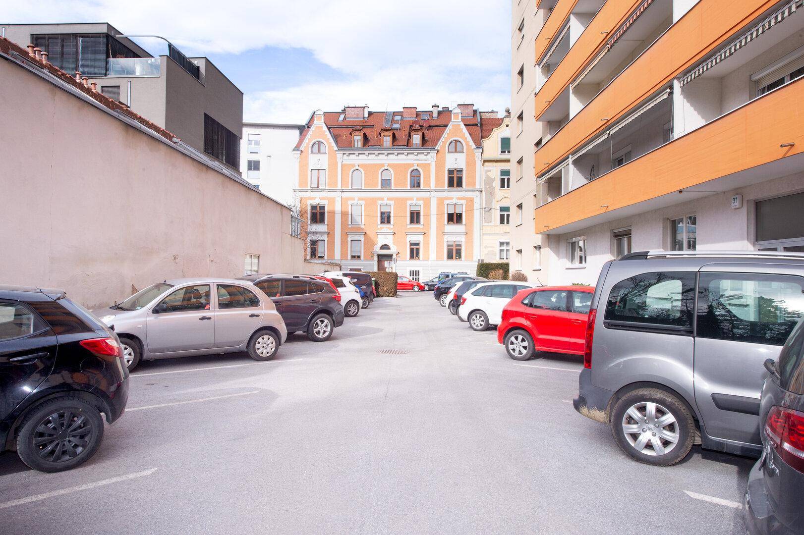 Außenparkplatz mit mehreren Autos und Blick auf ein historisches Gebäude im Hintergrund.