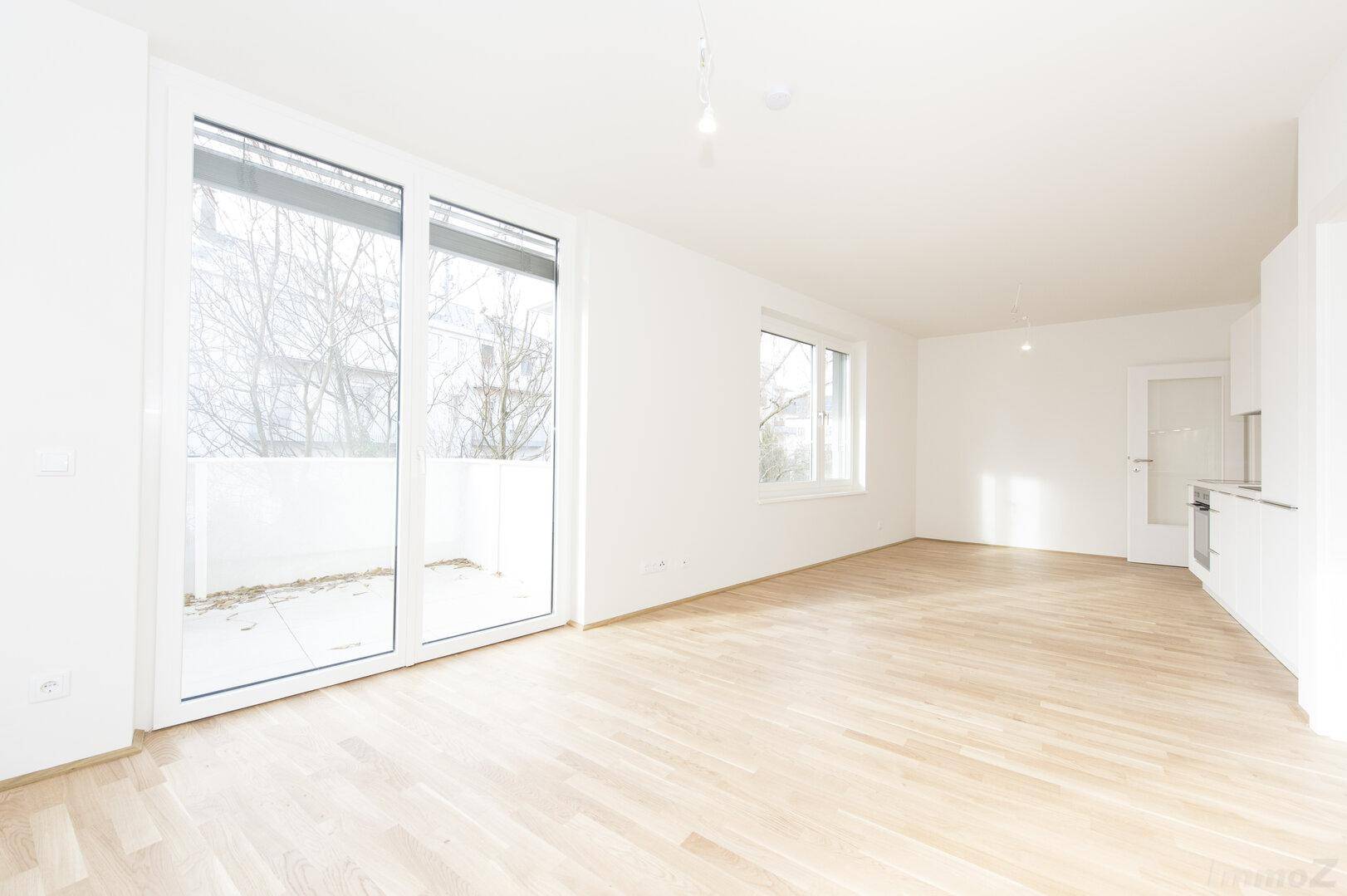 Geräumiger, heller Wohnbereich mit Parkettboden und großen Schiebetüren zum Balkon.