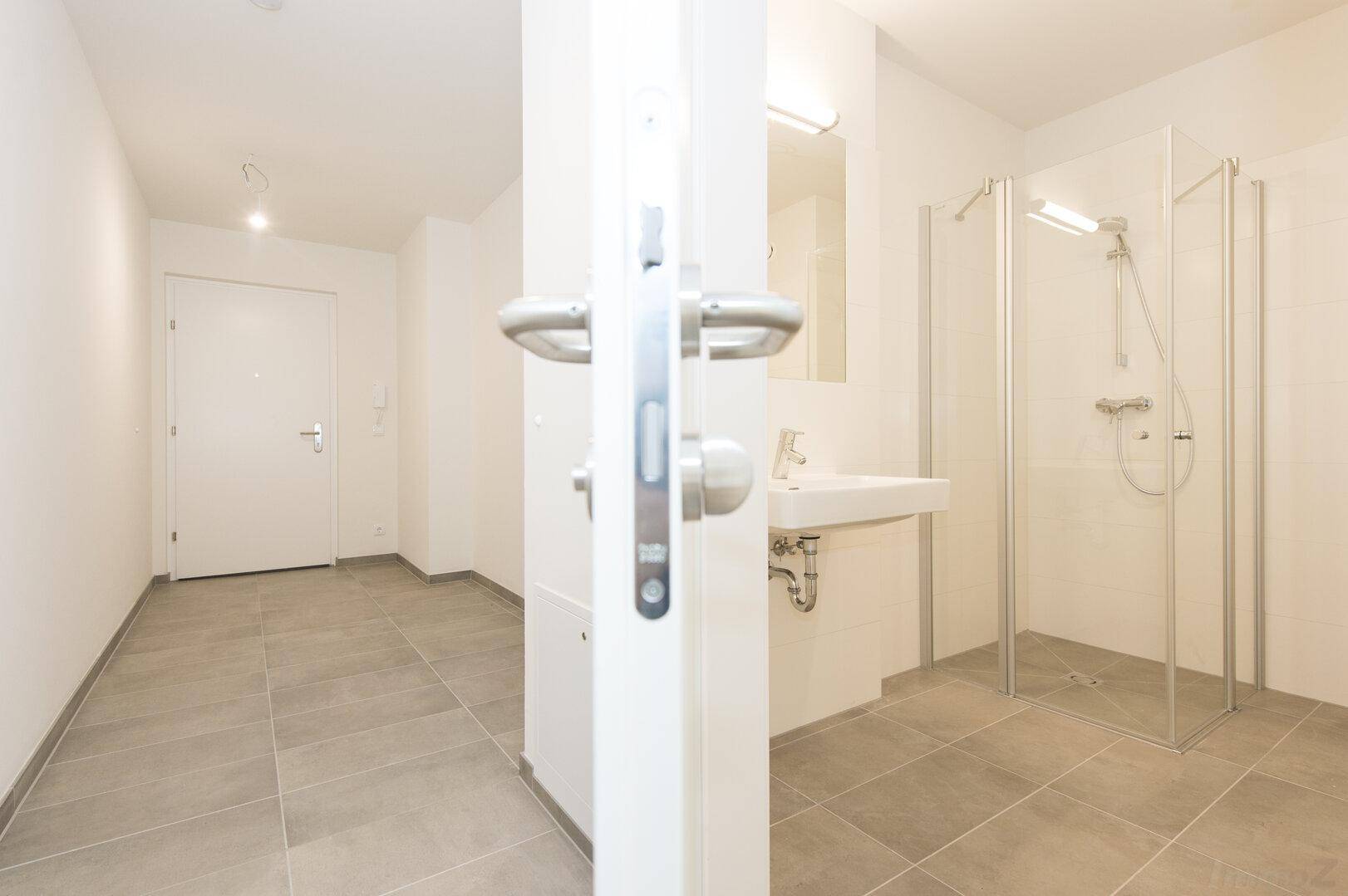 Heller Flur mit Fliesenboden und Blick in ein modernes Badezimmer mit Dusche.