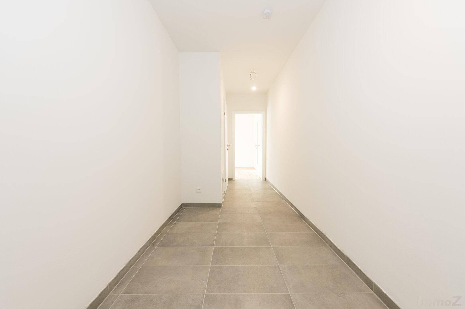 Schmaler, heller Flur mit modernen grauen Fliesen und weißen Wänden.