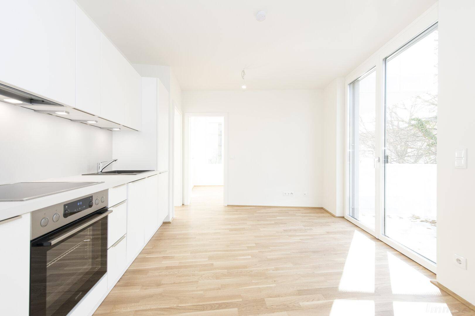 Moderne Einbauküche in Weiß mit Backofen, Induktionskochfeld und hellem Holzfußboden.