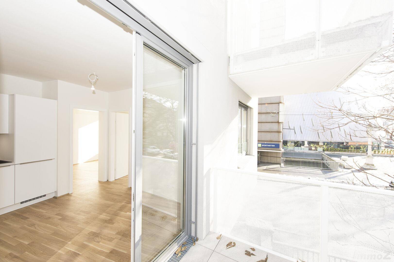 Heller Balkon mit Fliesenboden und Blick in einen modernen Wohnbereich mit weißer Küche.