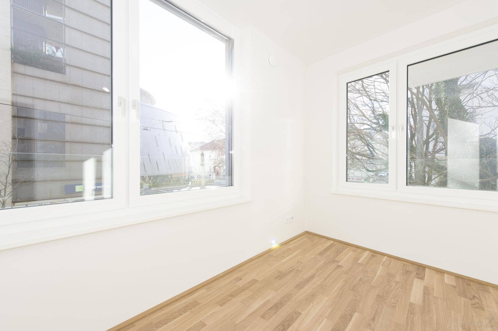 Heller Raum mit Holzfußboden und großen Fenstern, die viel Tageslicht hereinlassen.