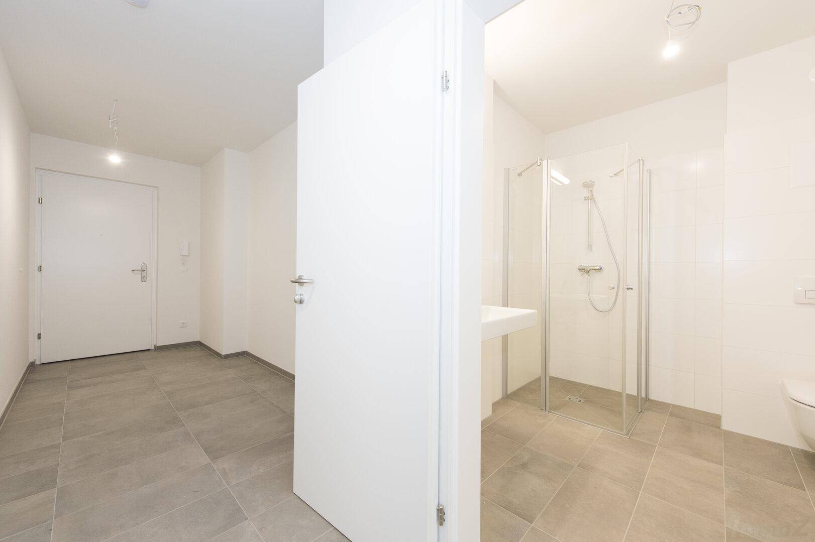 Modernes Badezimmer mit grauen Fliesen, weiß gefliesten Wänden und einer Duschkabine.