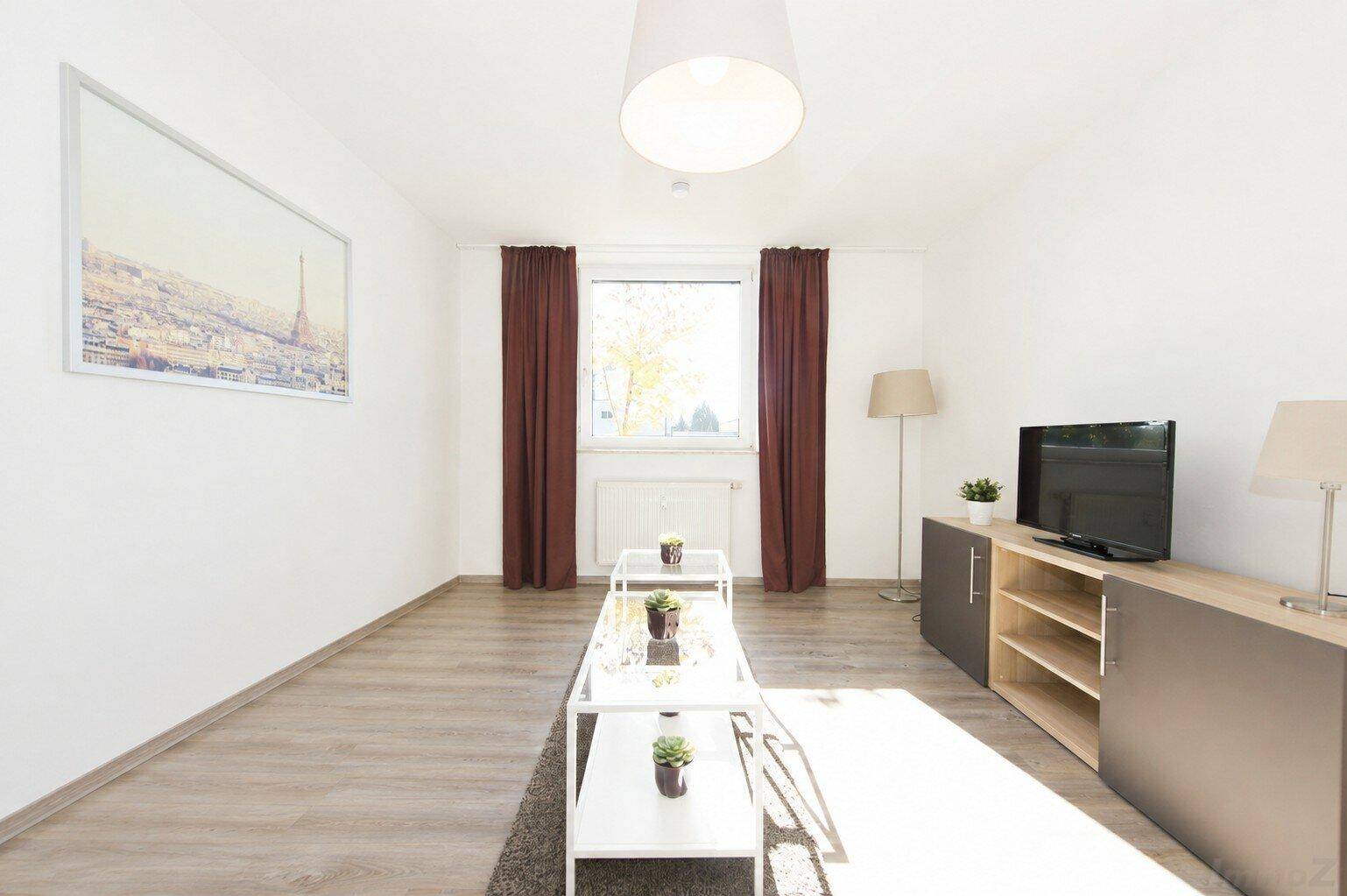 Heller Wohnbereich mit Laminatboden, großem Fenster und modernen Möbeln.