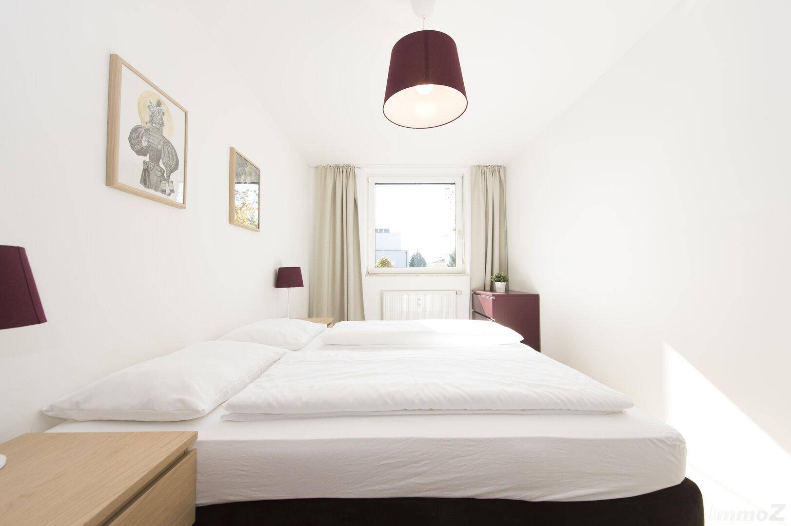 Helles Schlafzimmer mit Doppelbett, Nachttischen und Fenster mit Tageslicht.
