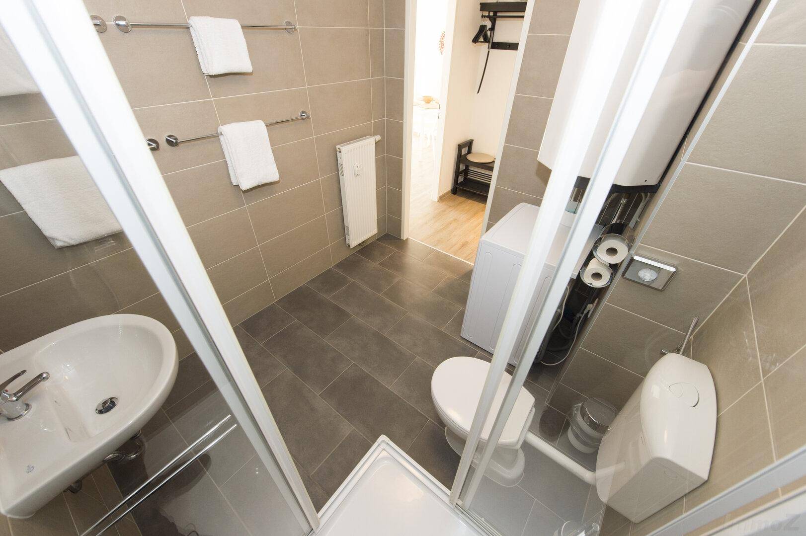 Modernes Badezimmer mit Dusche, WC, Waschbecken und Waschmaschine.