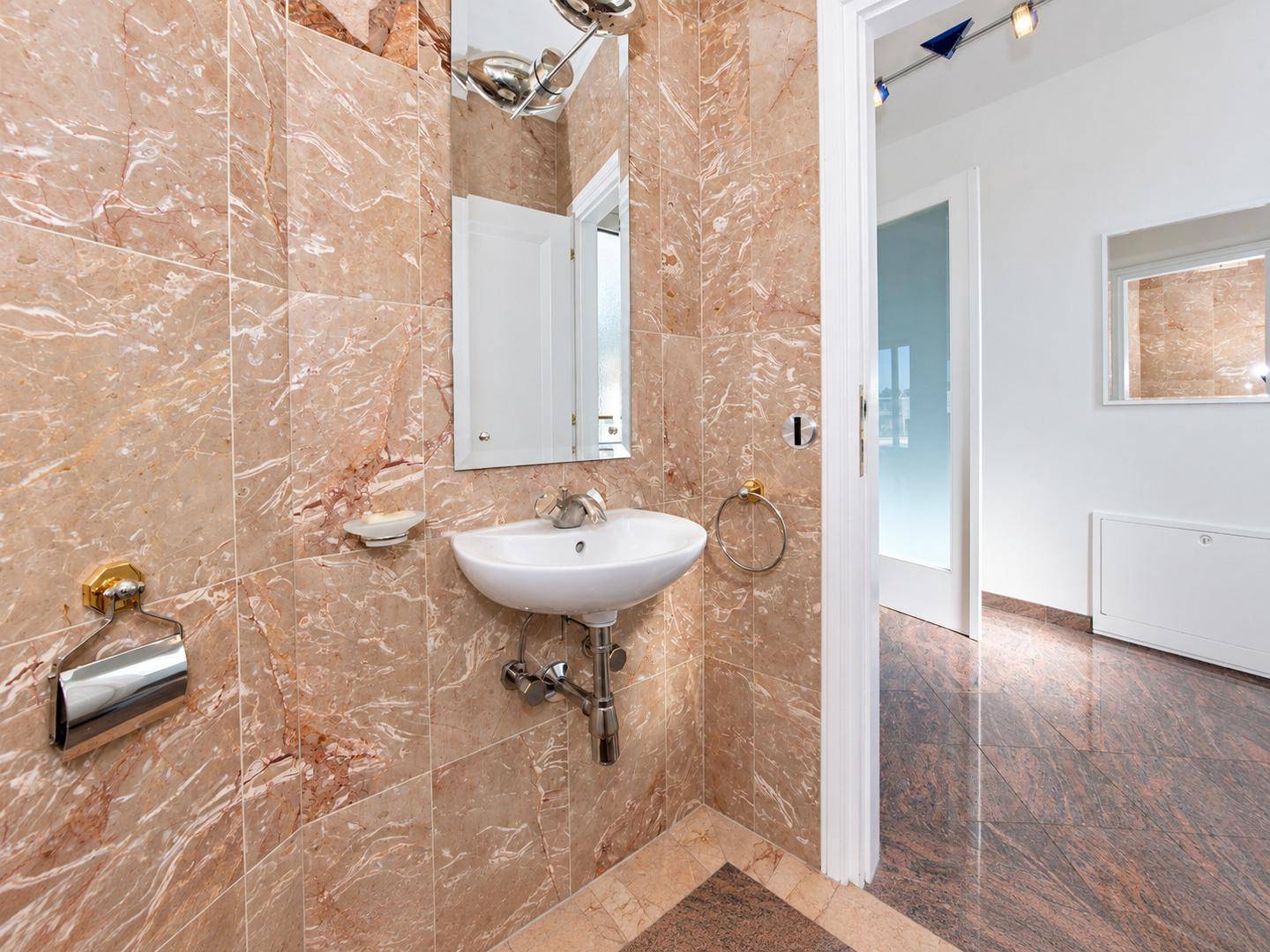 Modernes Gäste-WC mit Marmorfliesen, kleinem Waschbecken und Spiegel.