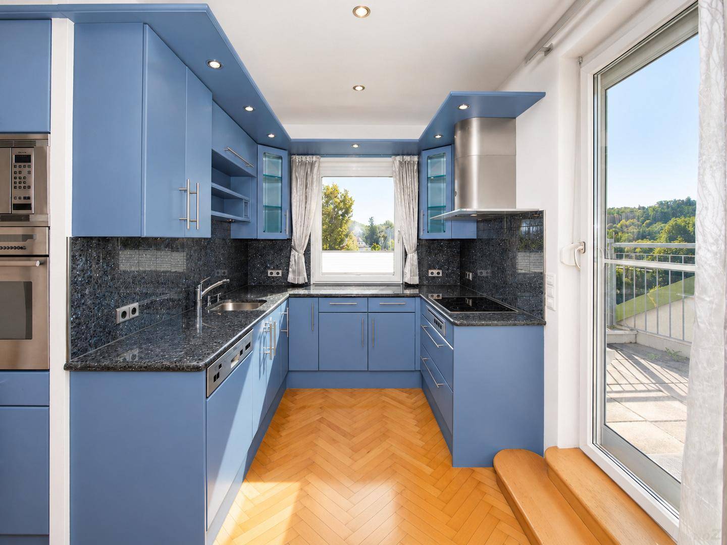 Moderne blaue Einbauküche mit Granitarbeitsplatten und Fenster mit Ausblick.