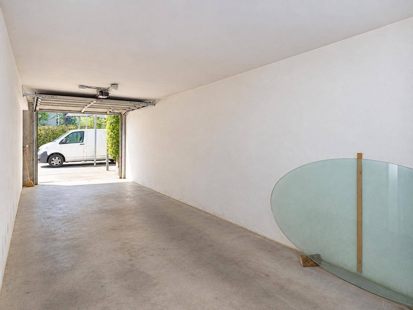 Helle Garage mit Betonboden und offenem Tor, ein Lieferwagen ist draußen sichtbar.