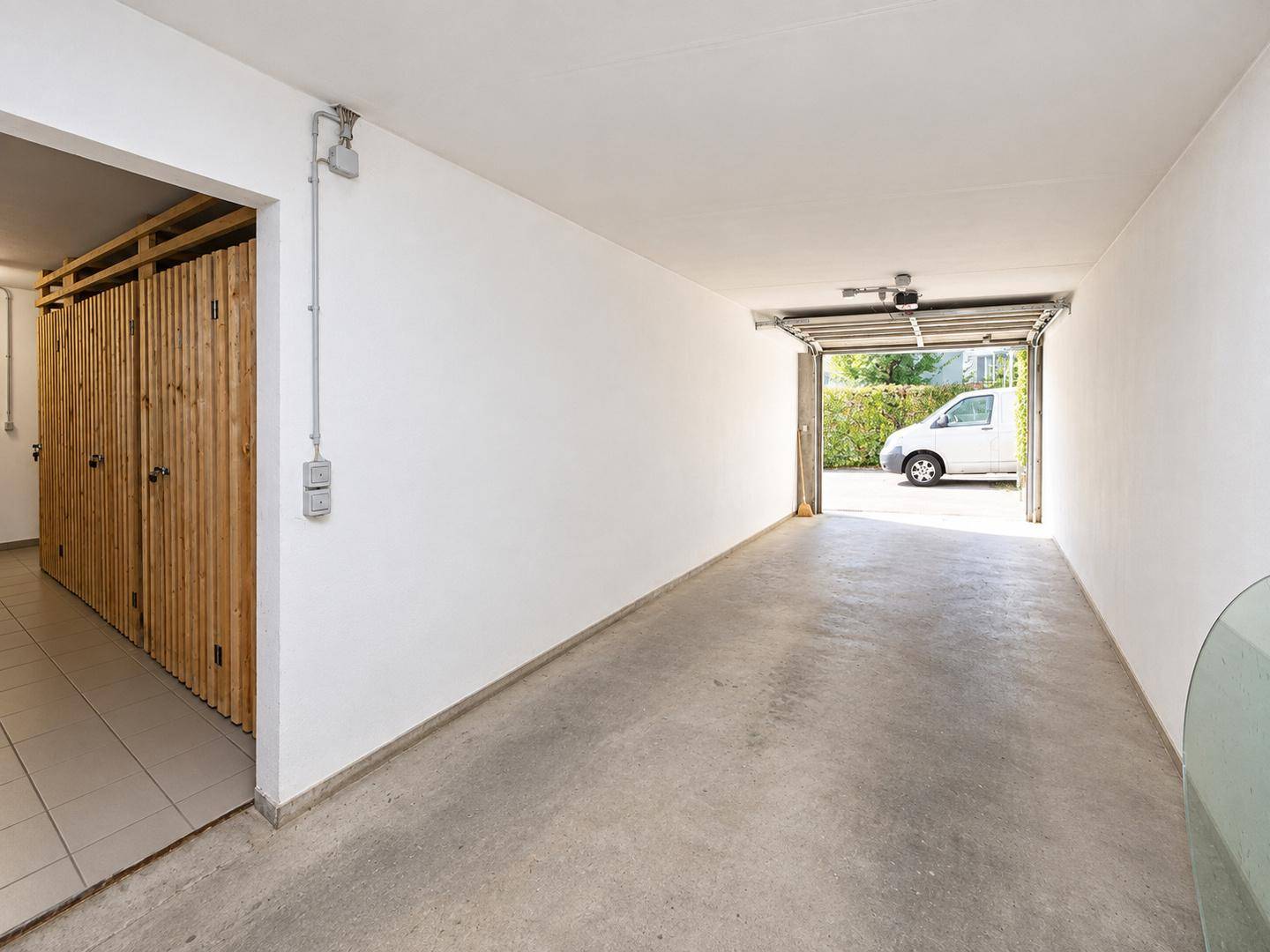 Geräumige Garage mit Betonboden, offenem Tor und praktischen Holz-Abstellräumen.
