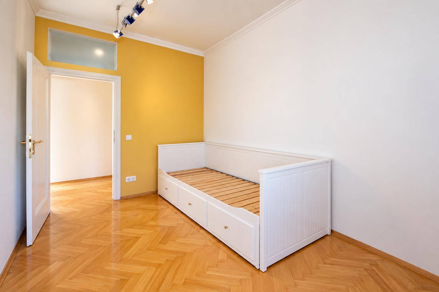 Helles Schlafzimmer mit Fischgrätparkett, Tagesbett und einer sonnigen gelben Akzentwand.