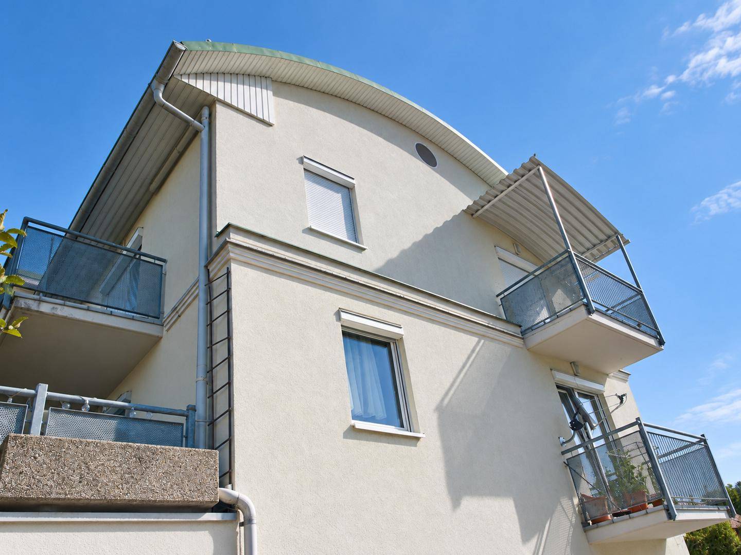 Moderne Gebäudefassade mit geschwungener Dachlinie, mehreren Balkonen und blauem Himmel.