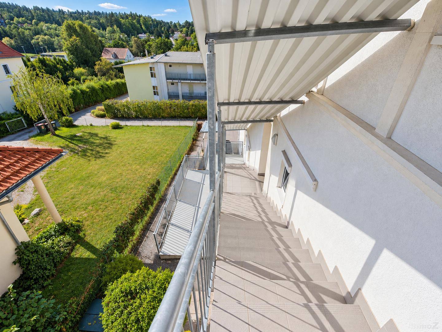 Außentreppe mit Metallgeländer und Blick auf den gepflegten Gartenbereich des Gebäudes.