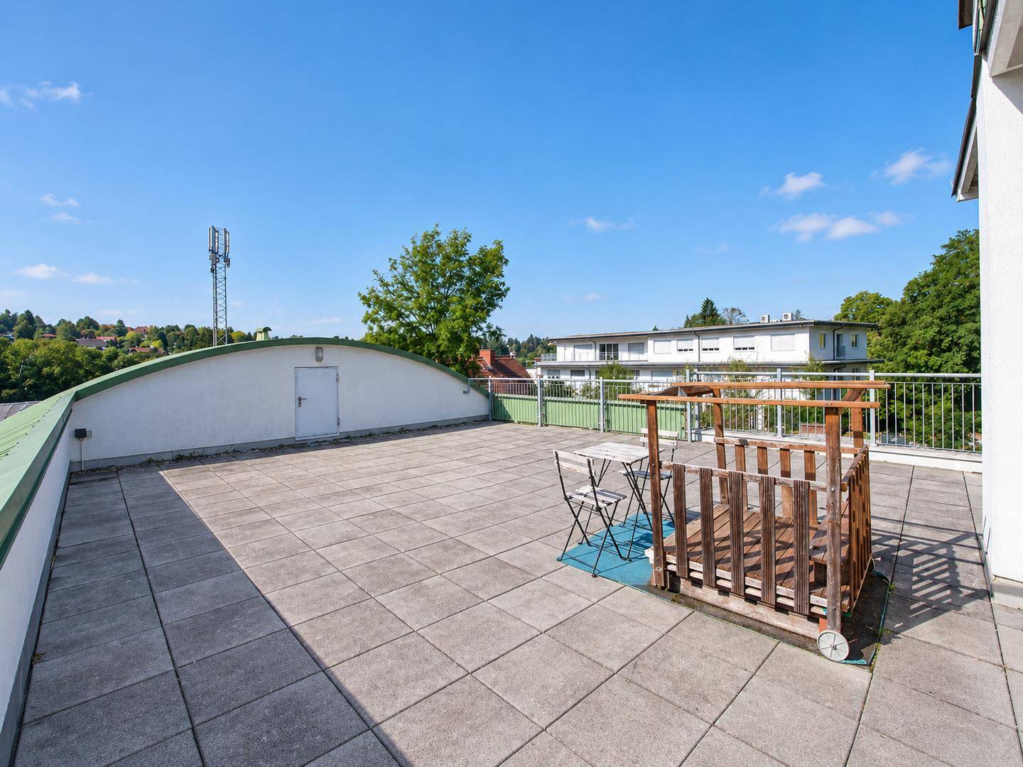 Große Dachterrasse mit Sitzgelegenheiten, Fliesenboden und Blick ins Grüne.