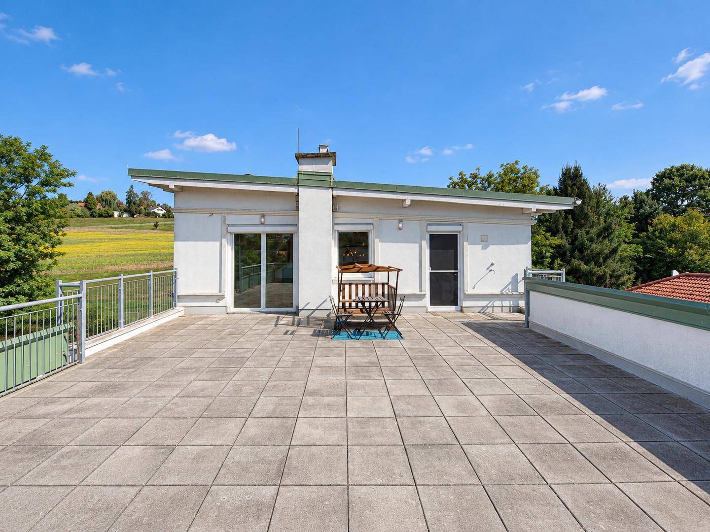 Sonniger Dachterrassenbereich mit Gartenmöbeln und weitem Blick ins Grüne.