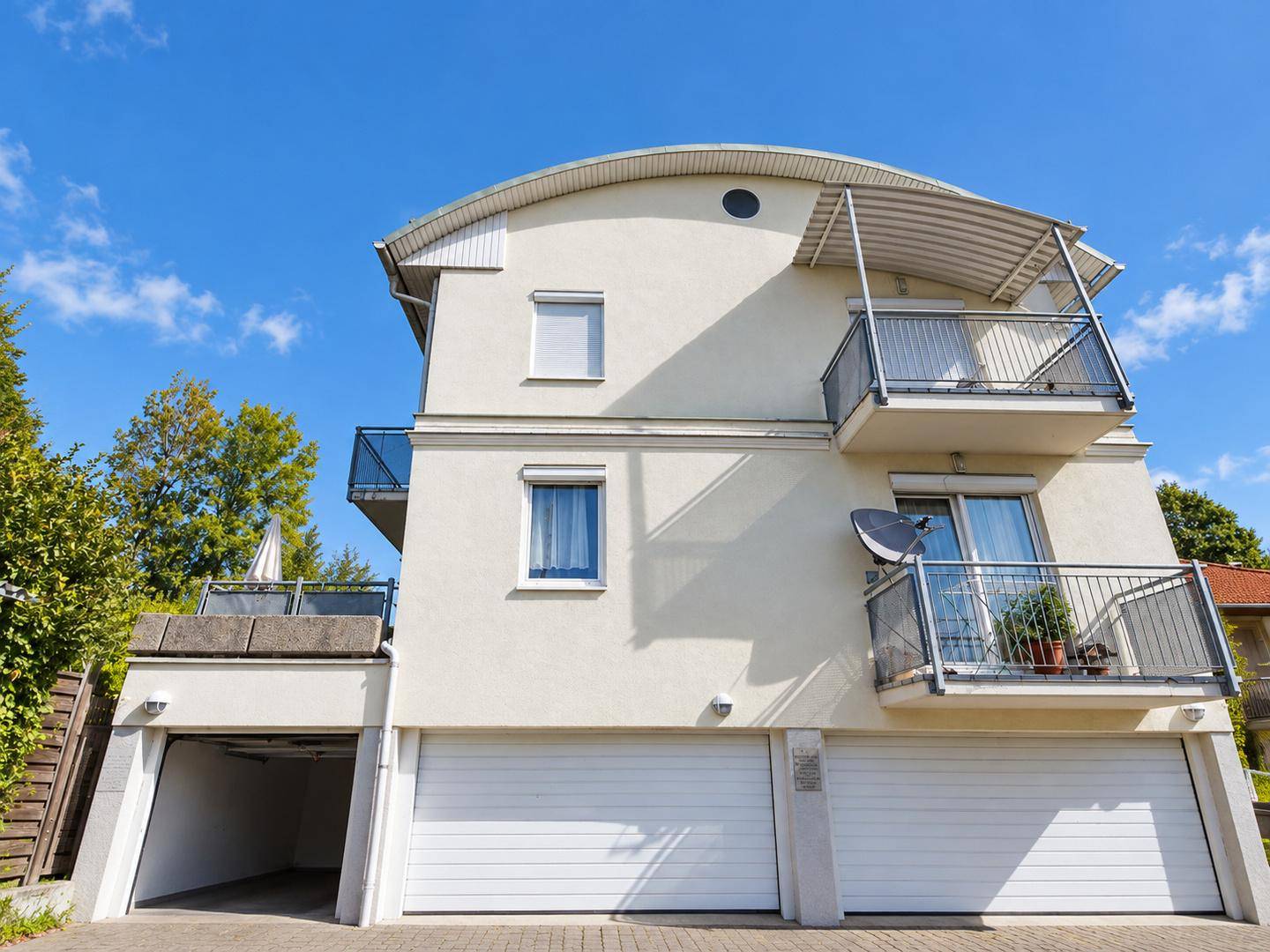 Ansicht der modernen Gebäudefassade mit Balkonen und zwei Garagentoren im Erdgeschoss.