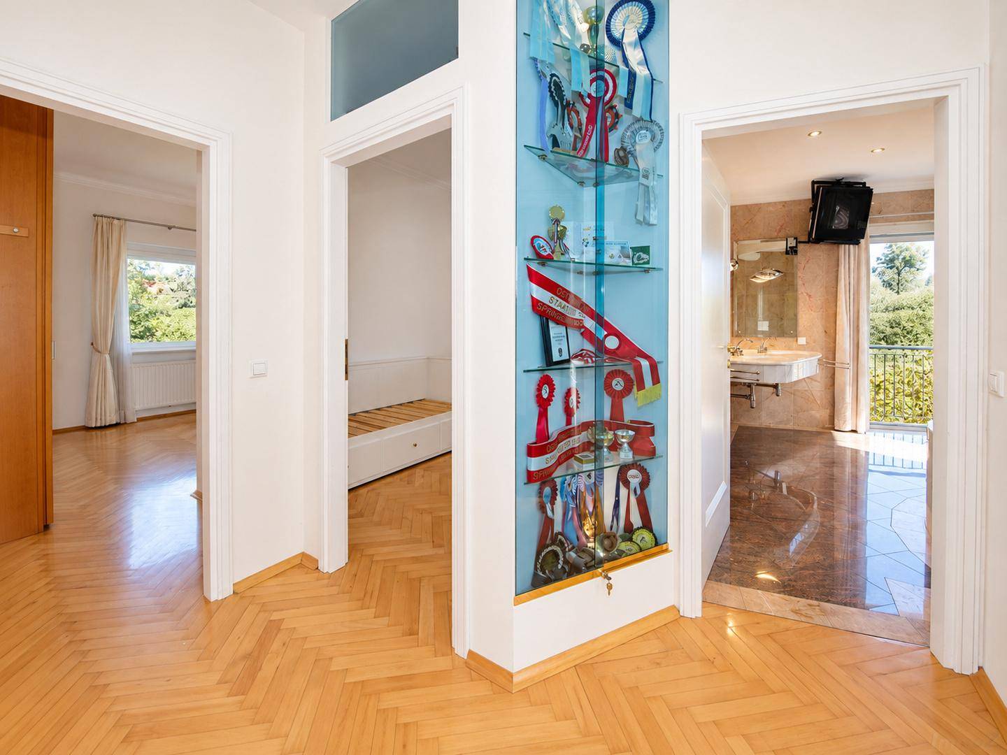 Geräumiger Flur mit Fischgrätparkett, beleuchteter Vitrine und Blick in angrenzende Zimmer.