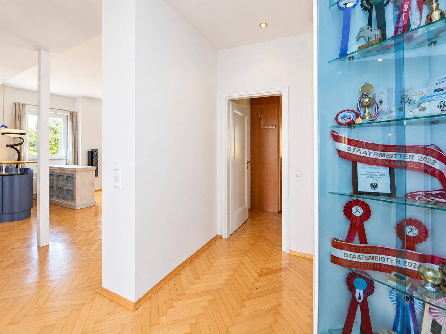 Heller Flur mit Fischgrätparkett und dekorativer Vitrine, die zu den Wohnbereichen führt.