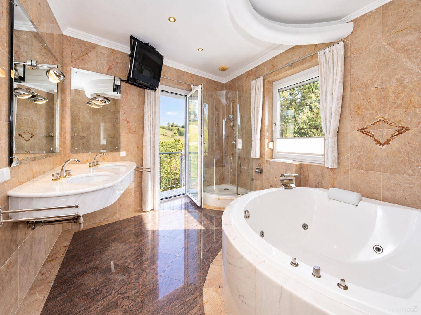 Luxuriöses Badezimmer mit Marmorfliesen, Whirlpool, Doppelwaschbecken und Balkonzugang mit Weitblick.