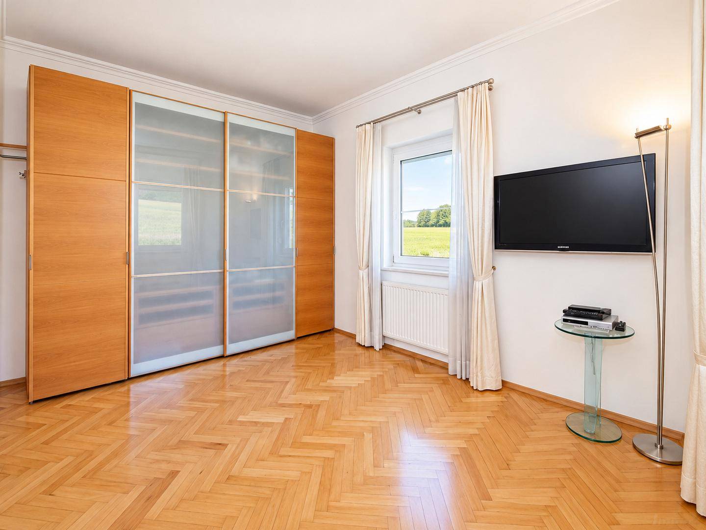 Geräumiges Schlafzimmer mit Fischgrätparkett, großem Einbauschrank und Fenster mit Ausblick.