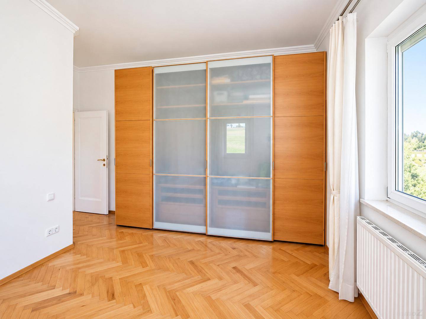 Schlafzimmer mit elegantem Fischgrätparkett und einem praktischen, raumhohen Einbauschrank.