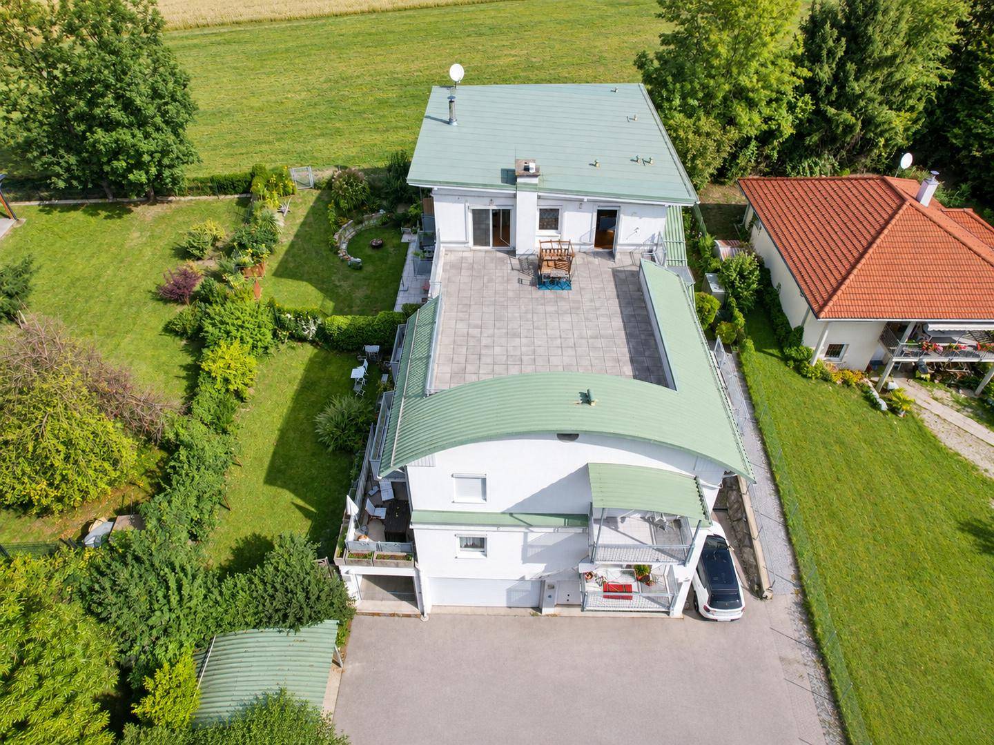 Weitläufige Luftaufnahme des Hauses mit großer Dachterrasse und umliegender Landschaft.