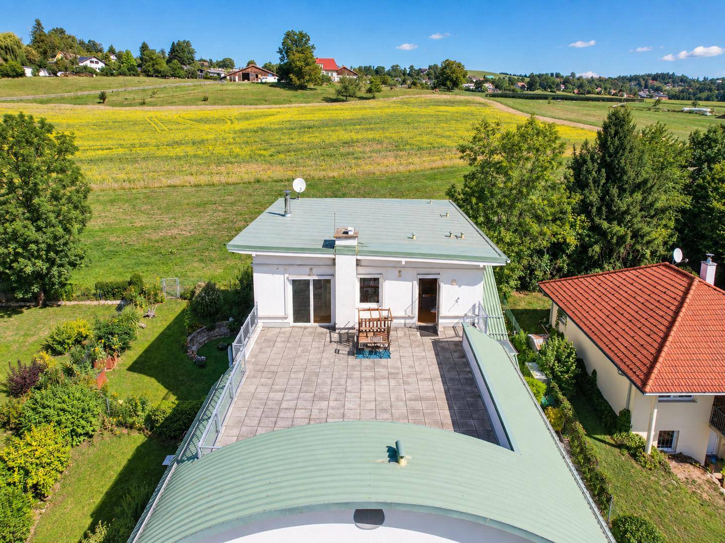 Luftaufnahme einer Immobilie mit großer gefliester Dachterrasse und weitem Blick ins Grüne.