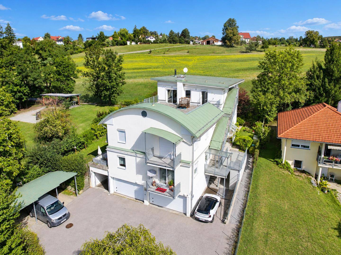 Luftaufnahme des Anwesens mit Gebäude, Garten, Carport und weitem Blick auf grüne Hügel.