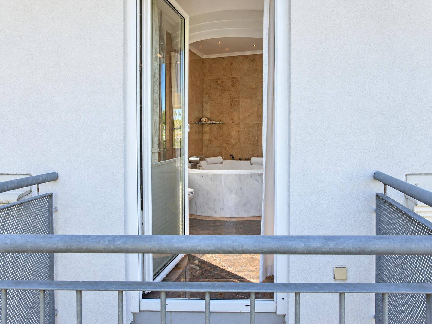 Blick vom Balkon in das luxuriöse Badezimmer mit Whirlpool und Marmoroberflächen.