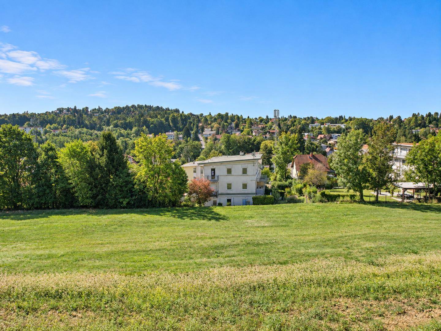 Das Anwesen aus der Ferne über ein weites grünes Feld mit Hügeln und einer Stadt im Hintergrund.