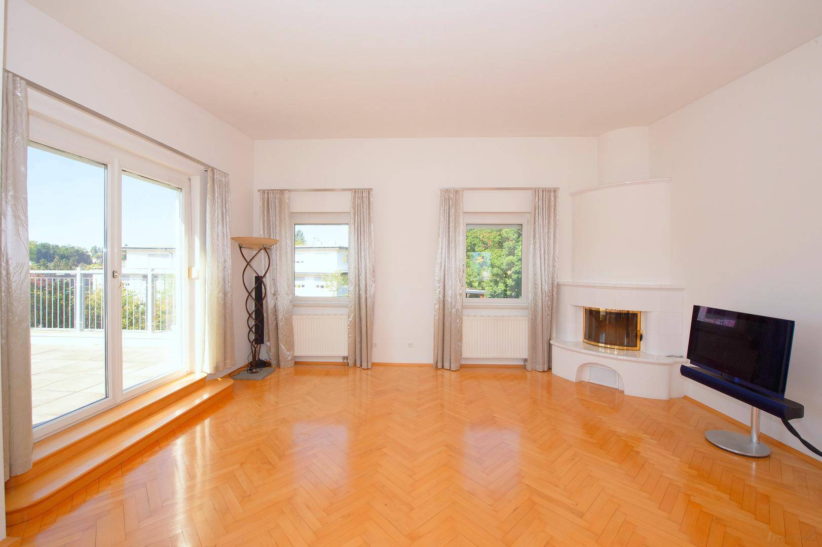 Helles Wohnzimmer mit Kamin, Parkettboden und großem Zugang zur Terrasse.