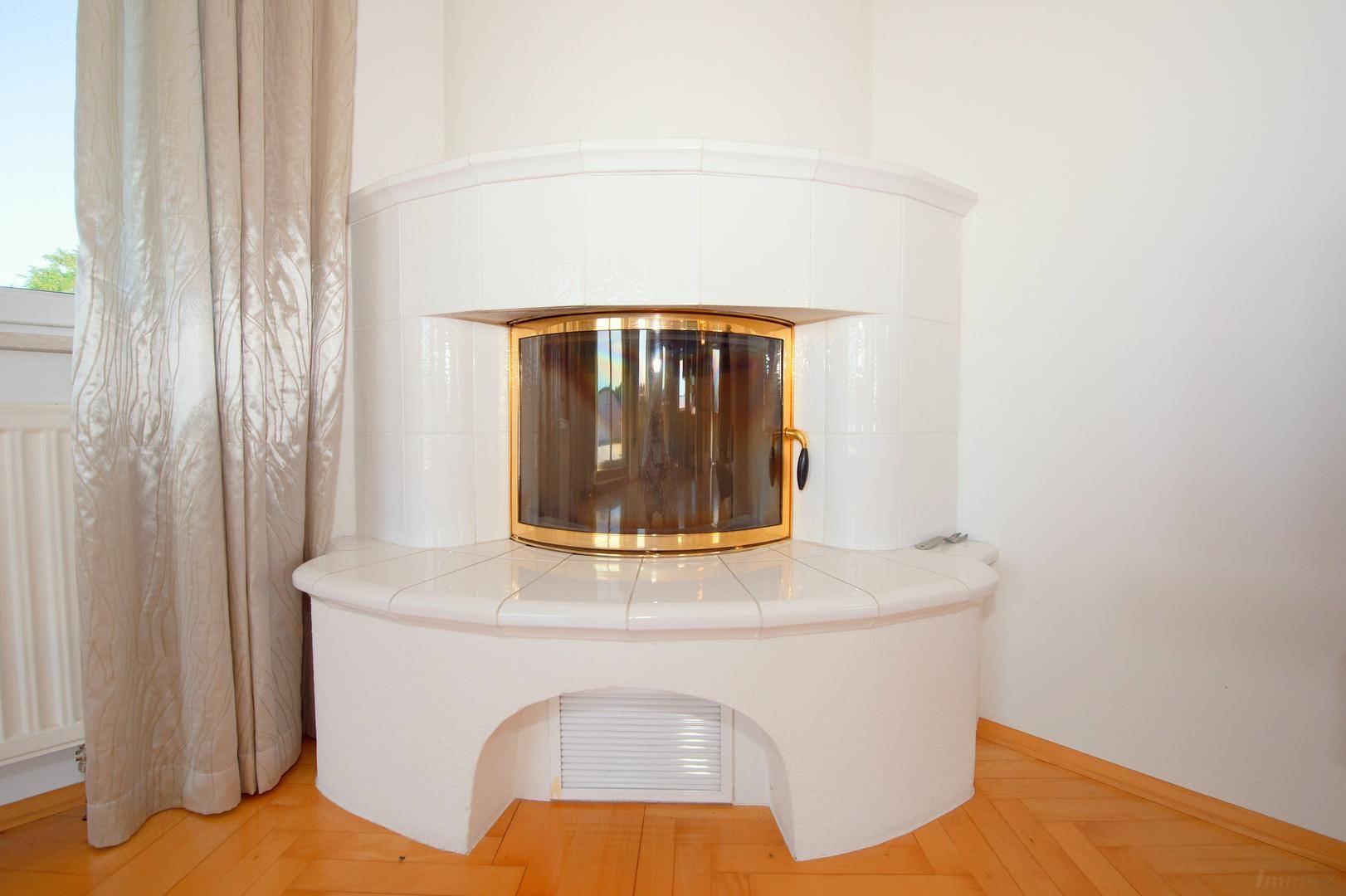 Gemütlicher Kamin im Wohnzimmer mit weißer Fliesenverkleidung und goldener Tür.